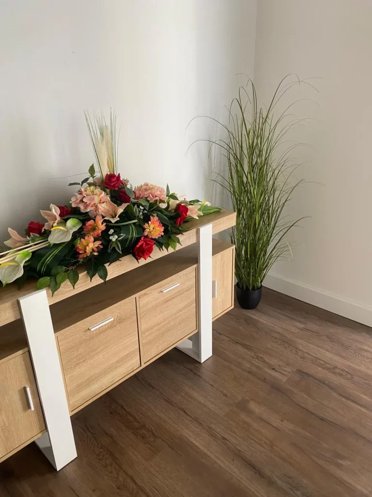 Composition florale de deuil posée sur un meuble en bois clair.