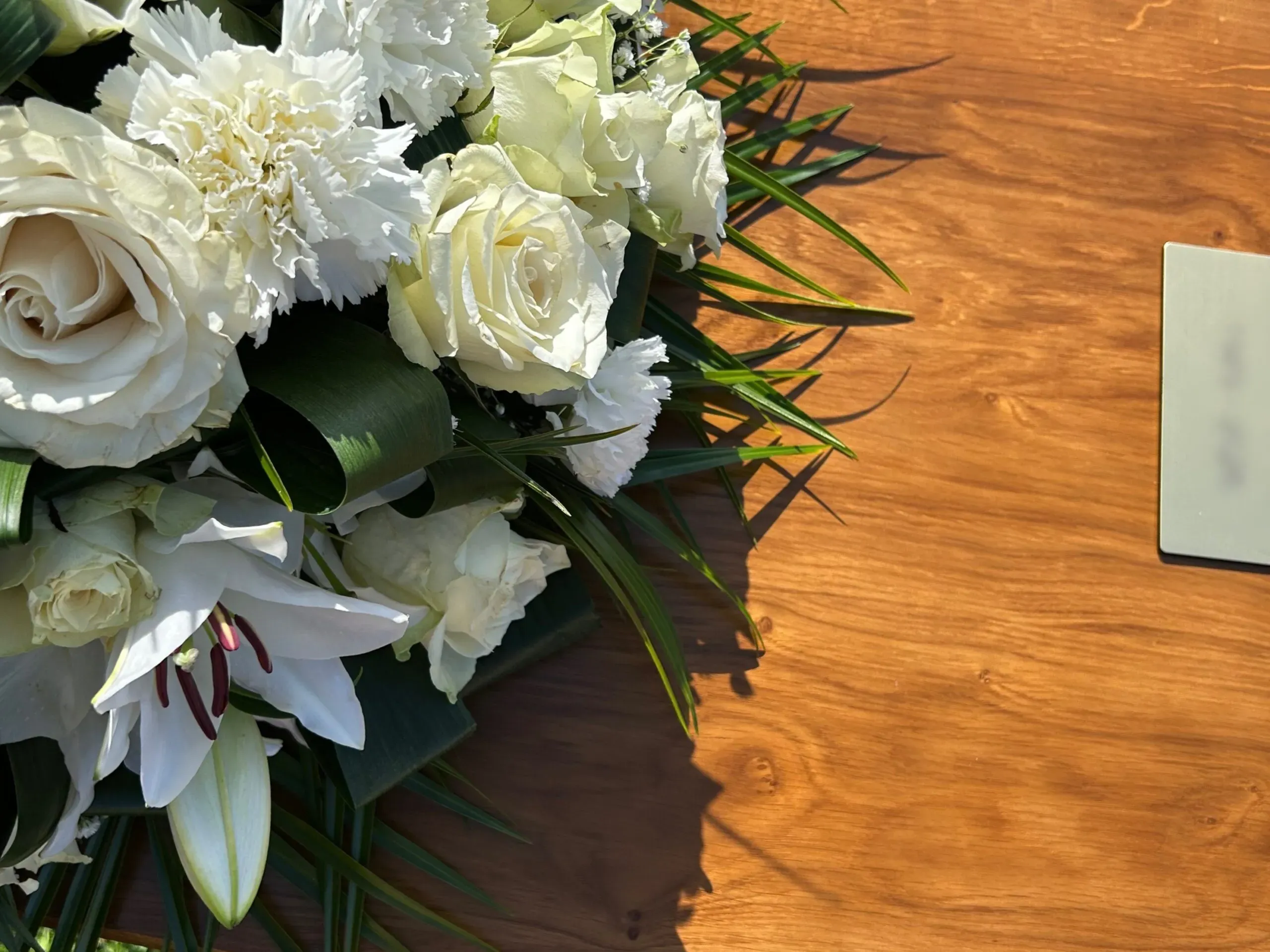 Dessus de cercueil en bois garni d'une composition de lys et roses blanches.