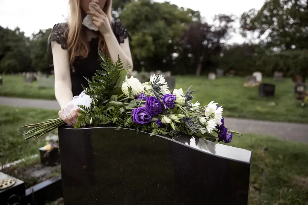 Femme en deuil déposant un bouquet de fleurs sur une pierre tombale au cimetière.
